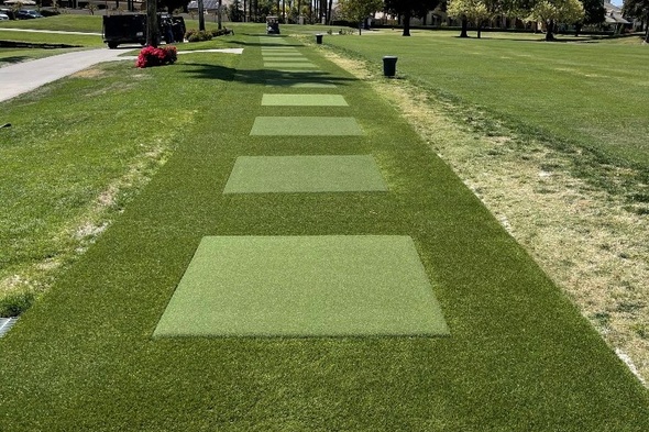 Outdoor tee line with light green synthetic grass boxes inside a dark green synthetic grass strip